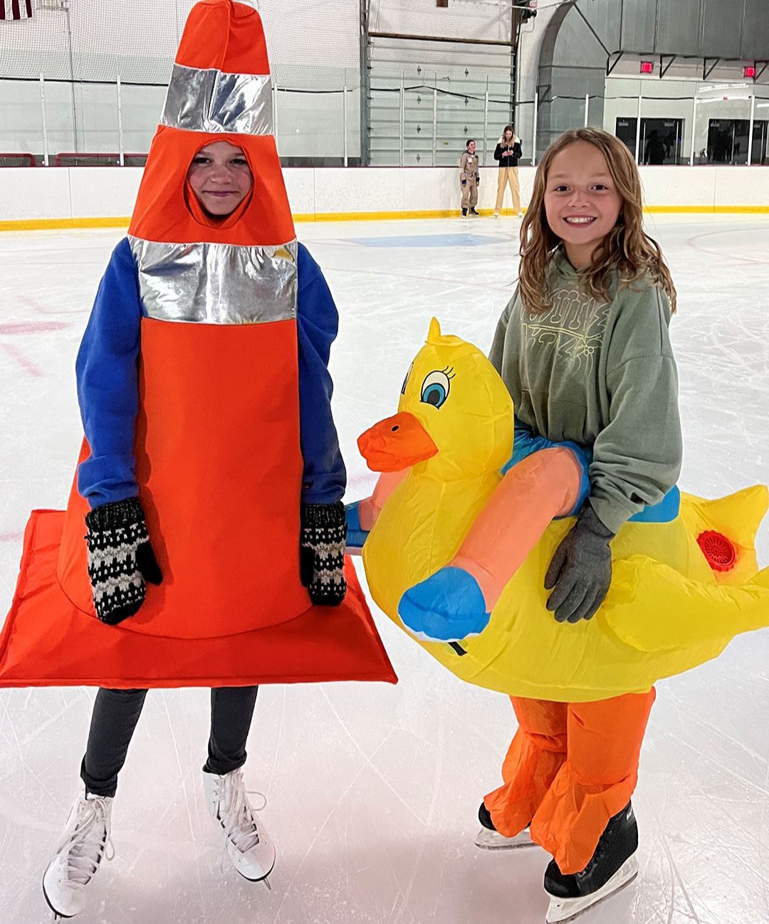 Photo of kids in Halloween costumes on skates - 1 as a safety cone and the other riding a duck