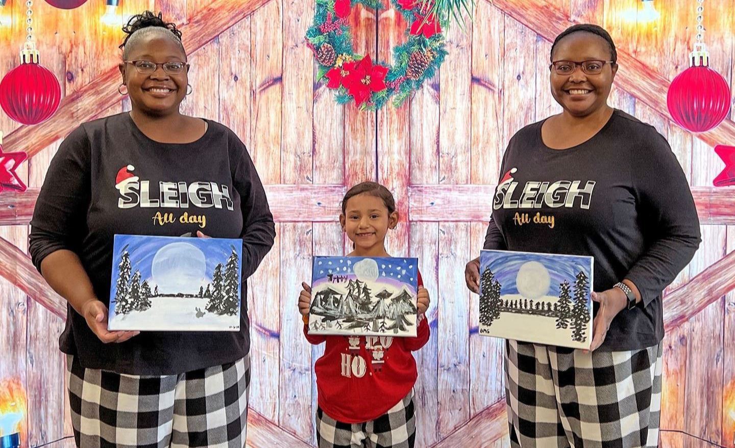 Photo of a family dressed in PJs posing with their paintings